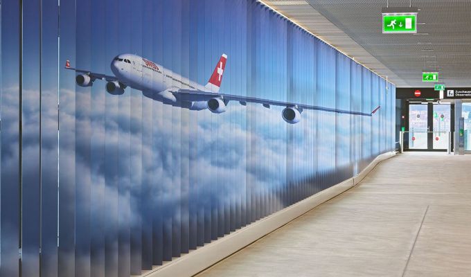 Feststehende Aluminiumlamellen sind die Träger der beiden riesigen Bilder im Zugangskorridor zur neuen Zuschauerterrasse am Dock B des Flughafens Zürich.